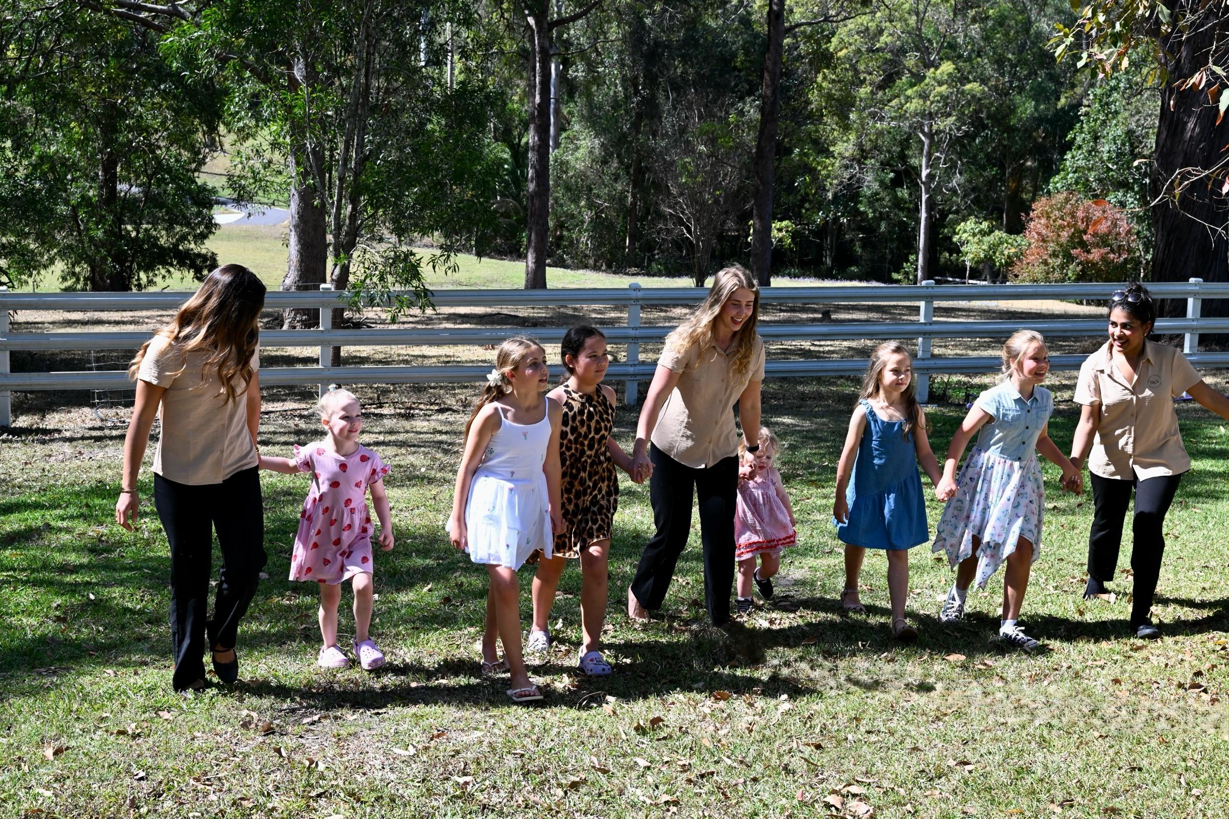 Children and carers walking hand in hand across a sunlit lawn