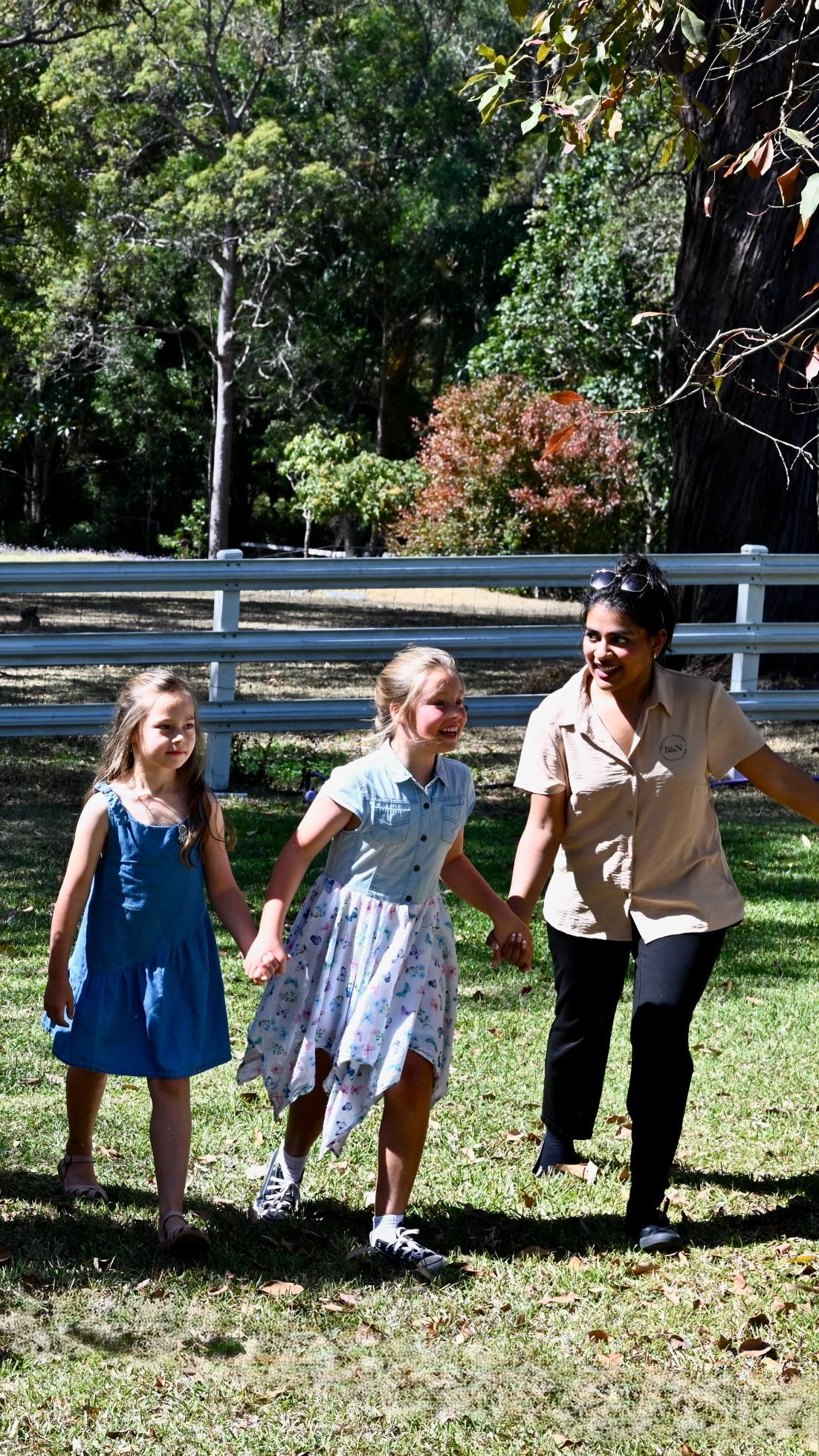 Two girls and a carer walking hand in hand across a sunny lawn