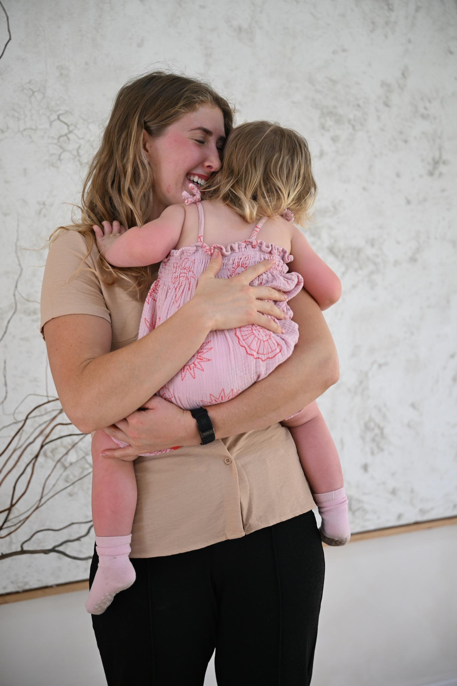 A nanny holding a toddler close, faces turned away, in front of a large textured artwork